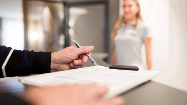 Hand mit Stift im Vordergrund, dahinter unscharf eine Frau