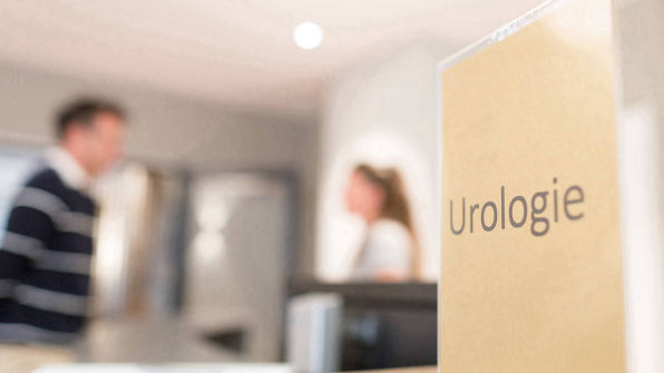 Schild Urologie, unscharf zwei Menschen im Hintergrund